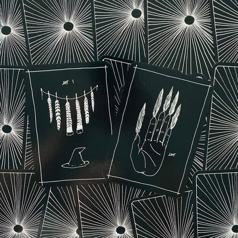 Tarot kortos juodame variante su baltomis iliustracijomis — dvi atverstos kortos (delno su plunksnomis ir vabzdžių gaudyklės motyvai) ant spinduliuotės raštuoto nugarėlių fono