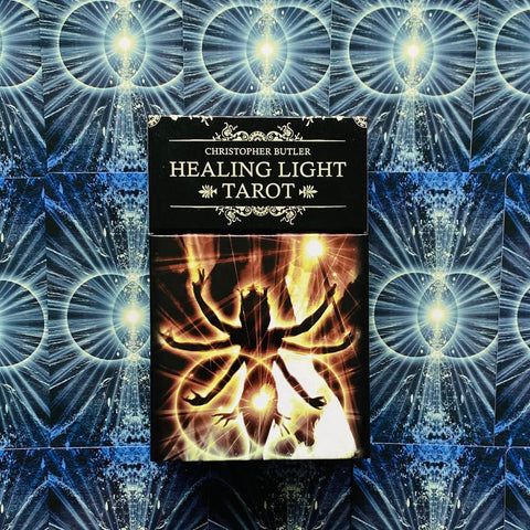 Healing Light tarot kortos Christopher Butler, juodas dėklas su švytinčia daugiasparne figūra ant mėlyno ornamentuoto fono