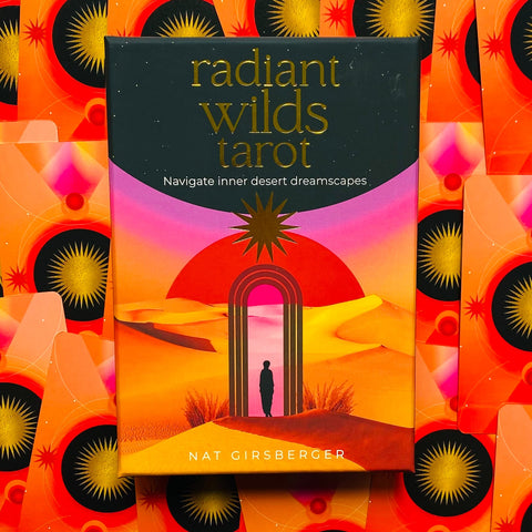 Tarot kortos Radiant Wilds (Nat Girsberger), ryški oranžinė‑rožinė dėžutė nuo aukšto kampo, matomos kortų nugarėlės su auksinėmis saulėmis