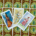 tarot kortos su auksiniu ir žalsvu ornamentu nugarėlių fone, trys atverstos kortos su skirtingomis figūromis iš viršaus matomos