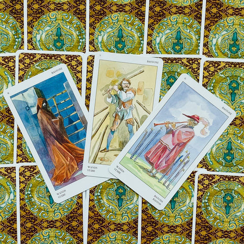 tarot kortos su auksiniu ir žalsvu ornamentu nugarėlių fone, trys atverstos kortos su skirtingomis figūromis iš viršaus matomos