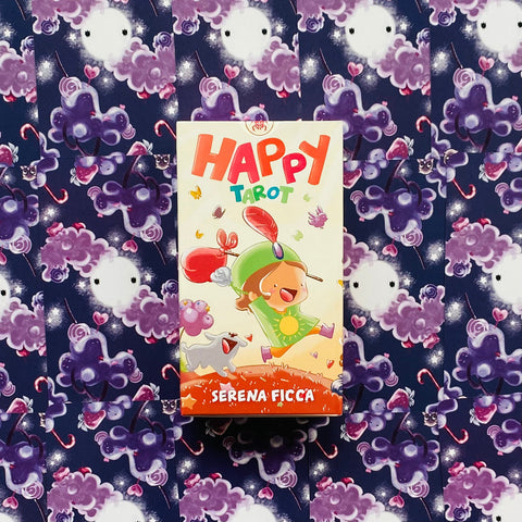 Happy Tarot kortos (Serena Ficca) priekinė spalvinga dėžutė su linksmu piešiniu, centre ant violetinio debesų fono