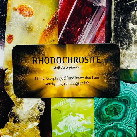 Rhodochrosite kortelė su afirmacija apie savęs priėmimą, ryškus auksinis fonas ant spalvotų kristalų