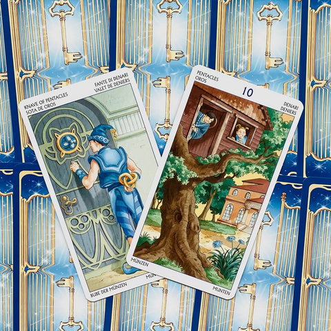 Tarot kortos su mėlynomis nugarėlėmis ir auksiniais raktais, dvi atverstos — jaunuolis prie durų ir medyje namelis, Pentaklių variantai