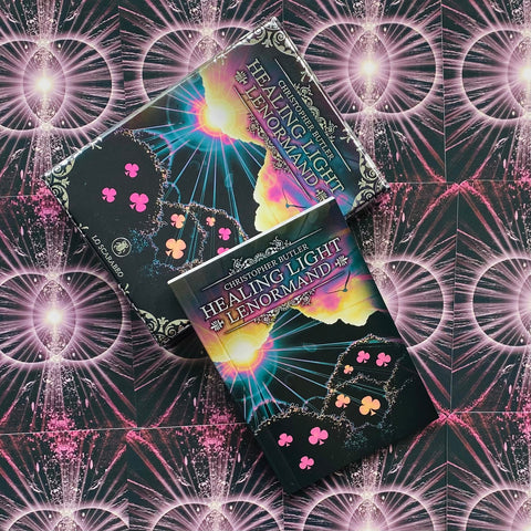 Lenormand kortos Healing Light su juoda blizgia dėkle ir rožiniais klubų simboliais, dvi dėžutės sluoksniuotos ant kosminio fono