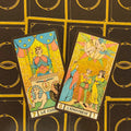 tarot kortos su auksiniu blizgiu paviršiumi, dvi atvertos kortos (Vežikas ir Meilužiai) iš arti, juodo fono su aukso raštais nugarėlių detalė