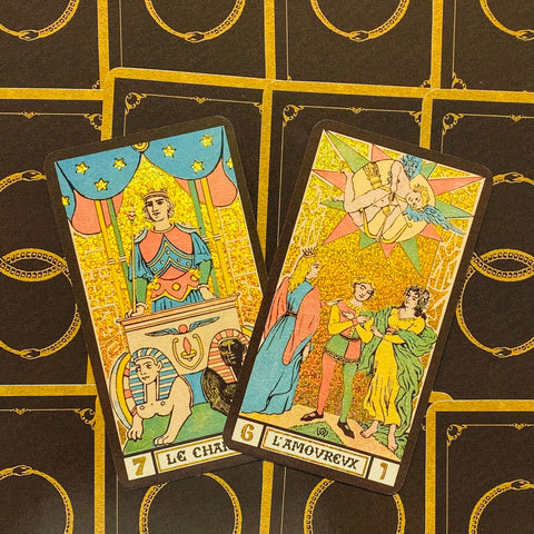 tarot kortos su auksiniu blizgiu paviršiumi, dvi atvertos kortos (Vežikas ir Meilužiai) iš arti, juodo fono su aukso raštais nugarėlių detalė