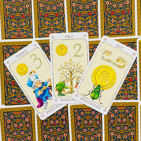 Tarot kortos Pentacles: trijų kortų rinkinys su kreminiu frontu, auksinėmis monetomis, žaliu vabzdžiu ir ornamentuota nugarėle