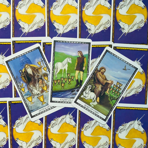 Tarot kortos Rider–Waite stiliaus rinkinys, trys atverstos taurės kortos ant violetinių vienaragių nugarėlių, parodyta detaliai