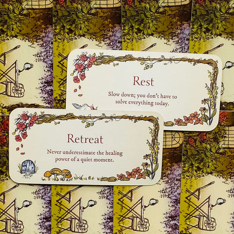 Kortelės su teigiamais pranešimais — dvi baltos su gėlių rėmeliais ir tekstais 'Retreat' ir 'Rest', skirtos ramybės praktikoms, parodytos ant raštuoto fono