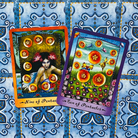 tarot kortos, artimas dviejų kortų komplektas: devynios ir dešimt pentaklų su oranžiniu ir violetiniu rėmeliu ant mėlyno raštuoto audinio