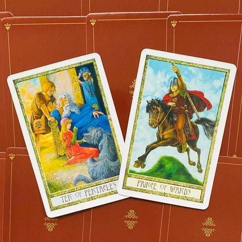 Tarot kortos atvertos dviem: Ten of Pentacles ir Prince of Wands ant raudono ornamentuoto fono, padėtos iš viršaus kampu.