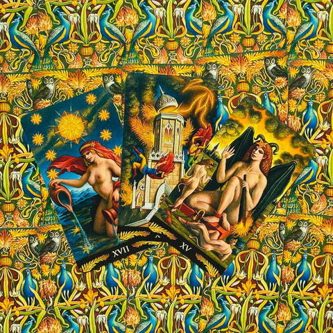 Tarot kortos — trijų Didžiųjų Arkana kortų fanuotas išdėstymas ant ryškios geltonai‑mėlynos ornamentuotos medžiagos