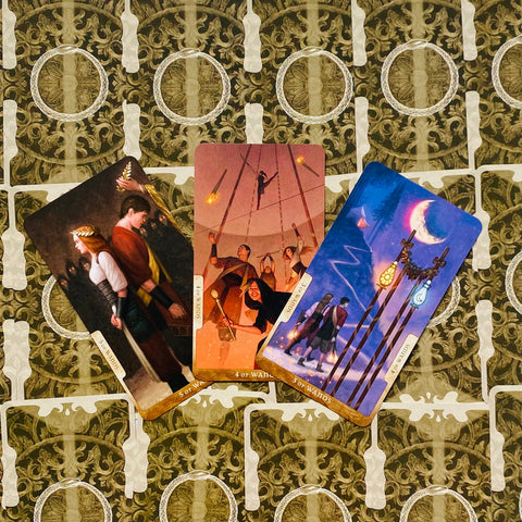 tarot kortos trys atvertos lazdų kortos su ryškiomis iliustracijomis, išdėstytos vėduoklėje ant žalio ornamentuoto nugarėlės fono
