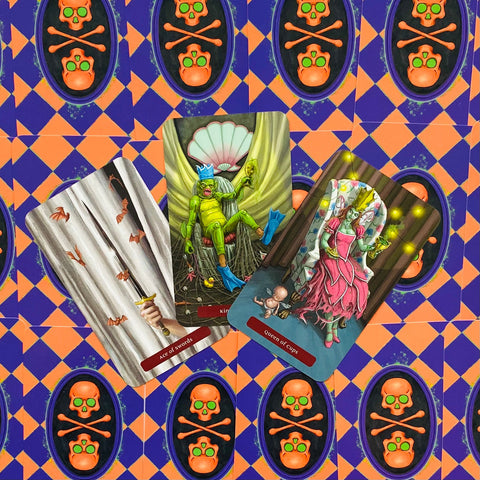 Tarot kortos ant oranžinio–violetinio kaukolės rašto fono — trys atverstos kortos su sodriomis iliustracijomis