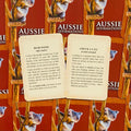 Aussie afirmacijų kortelės, dvi atverstos kreminės kortos su tekstais Bush Week ir Chuck a U-ey prieš raudoną dėžutę su koala