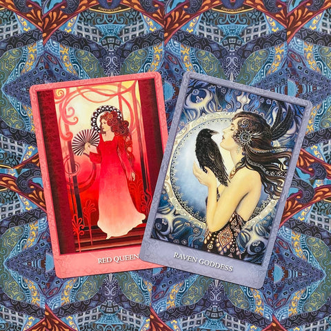 Orakulo kortos — dvi demonstracinės kortos Red Queen (raudona) ir Raven Goddess (mėlyna), pasuktos ir persidengusios ant ornamentuoto audinio fono