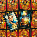 Tarot kortos su raudonomis auksuotomis nugarėlėmis, dvi atverstos kortos kampuotos: moteris su pakabuku ir moteris prie kristalinio gaubto