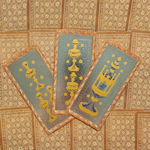 Tarot kortos su auksiniais ir mėlynais ornamentais, trijų kortų išdėstymas ant raštuoto rusvo fono, priekiai skirtingi