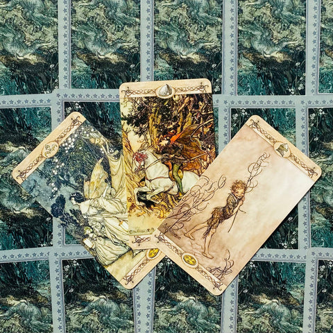 Tarot kortos su iliustracijomis, trys atverstos kortos fanuotos centre ant žalių ornamentuotų nugarėlių