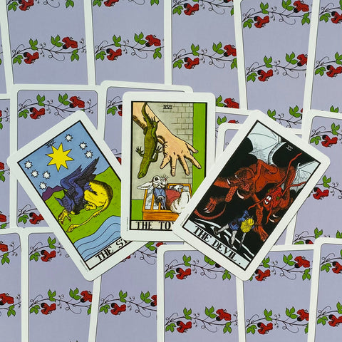 Tarot kortos – trijų atverstos Rider‑Waite kortos (Žvaigždė, Bokštas, Velnias) išdėstytos ant violetinės gėlėtos nugarėlės