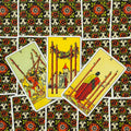 Tarot kortos Rider–Waite, trijų lazdelės kortos išdėstytos ant juodai-raudonai raštuotos nugarėlės, arti fotografuota