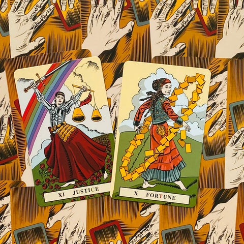 Tarot kortos Justice (XI) ir Fortune (X), spalvingas viršutinio plano poros išdėstymas ant rankų ir kortelių rašto fono