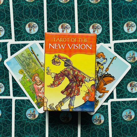 Produktų puslapyje — geltona „Tarot of the New Vision“ dėžutė centre su trimis išskleistomis kortomis ant žalsvai mėlyno raštuoto fono