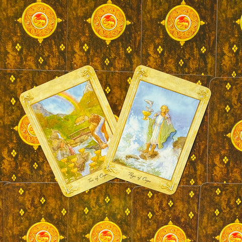 tarot kortos akvareliniais piešiniais — Ten of Cups ir Page of Cups atvertos ant rudos auksinės galinės pusės, demonstruoja taurų rūšį ir pavyzdinį išdėstymą