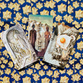 Tarot kortos komplektas — trys iliustruotos kortos iš Rider‑tipo kaladės išdėstytos ant mėlyno audinio su auksinėmis žvaigždėmis