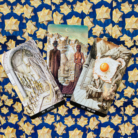 Tarot kortos komplektas — trys iliustruotos kortos iš Rider‑tipo kaladės išdėstytos ant mėlyno audinio su auksinėmis žvaigždėmis