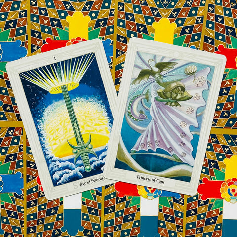 Tarot kortos Rider‑Waite stiliaus, dvi atvertos kortos (Ace of Swords ir Princess of Cups) ant dekoratyvios pakuotės
