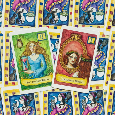 tarot kortos su iliustracijomis, dvi priekinės kortos — The Timeless Witch (žalia) ir The Ageless Witch (raudona), išdėstytos ant mėlynai geltonos nugarėlės