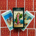 Produktų puslapyje — Tarot Lenormand dėžutė centre, dvi atviros kortos su žaliais rėmais ir raudonų nugarėlių fonas, pabrėžia dizainą ir kortų variantą
