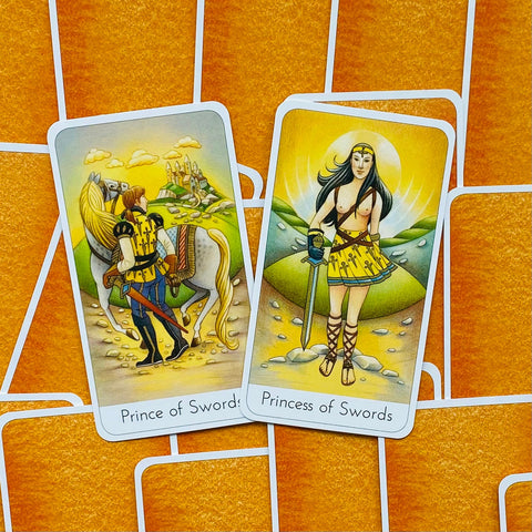 Tarot kortos su Prince ir Princess of Swords vaizdais, geltonos nugarėlės ir oranžinis tinklinis fonas