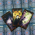 Tarot kortos su juodais rėmeliais, trijų kortų išklotinė su mistinėmis iliustracijomis ant mėlyno nugarėlių dizaino