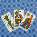 Tarot kortos Marselio stiliaus: trys spalvotos kortos (tūzas lazdų, karalius ir karalienė monetų) plokščiai ant mėlyno raštuoto audinio