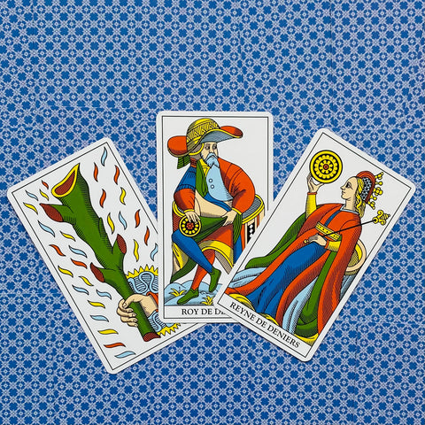 Tarot kortos Marselio stiliaus: trys spalvotos kortos (tūzas lazdų, karalius ir karalienė monetų) plokščiai ant mėlyno raštuoto audinio