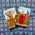 Tarot kortos Rider–Waite stiliaus, dvi kortos (Ten of Wands, Nine of Pentacles) ant mėlyno gėlėto fono, pasuktos kampu