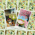Tarot kortos, dvi iliustruotos kortos (Nine of Earth Apple ir Nine of Water Peach) ant žalio gėlių fono, iš priekio