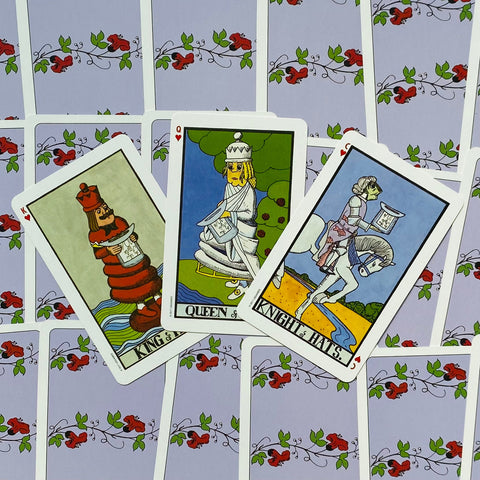tarot kortos su šviesiai violetiniu gėlėtu nugarėliu, trys išrikiuotos karališkos figūros – karalius, karalienė ir riteris