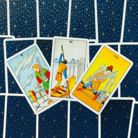 Tarot kortos Rider–Waite komplektas, trys kardų kortos (V, VI, VII) išdėstytos ventyse ant mėlyno žvaigždėto nugarėlio