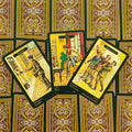 tarot kortos klasikiniu ornamentu nugarėlių fone, trys atverstos geltonai–žalsvos iliustruotos kortos matomos iš arti