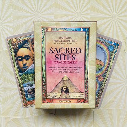 Orakulo kortos Sacred Sites: kompaktiška dėžutė su rožiniu viršeliu ir piramide, fone dvi spalvotos atverstos kortos