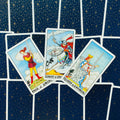 tarot kortos Rider–Waite stiliaus, trys kardų rūšies kortos (Page, Knight, Queen) išdėstytos virš tamsių žvaigždžių nugarėlių