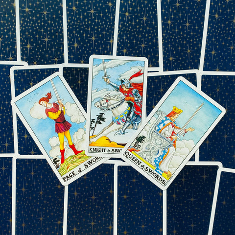 tarot kortos Rider–Waite stiliaus, trys kardų rūšies kortos (Page, Knight, Queen) išdėstytos virš tamsių žvaigždžių nugarėlių