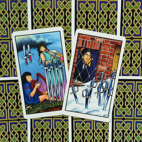 tarot kortos Rider–Waite stiliaus, dvi atviros kortos (VII ir VIII kalavijų) ant juoda‑auksinės nugarėlės