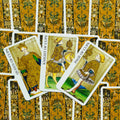 Tarot kortos su aukso rašto nugarėlėmis ir atvertomis Taurų kortomis — Karalienė, Riteris ir Puslapis matomi iš viršaus