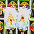 Tarot kortos — dvi auksinių lazdelės kortos ant balto debesuoto lauko, gulsčios ant ryškaus simbolių fono