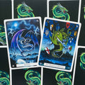 Tarot kortos drakonų tematikos: dvi atverstos kortos „Rebirth“ ir „The Wounded Dragon“ ant žalio nugarėlių fono